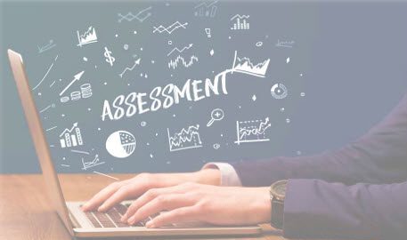 Employee typing on a laptop with the word assessment written on the board behind them